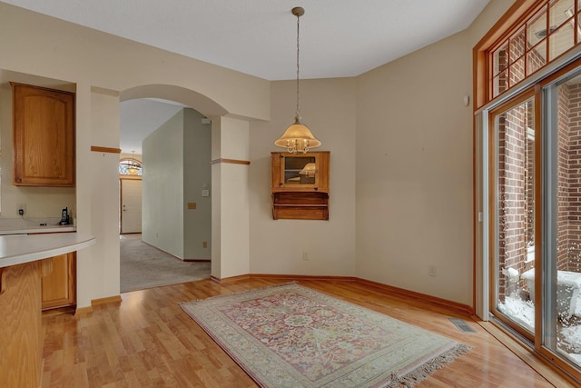 dining room featuring light wood finished floors, visible vents, arched walkways, and baseboards