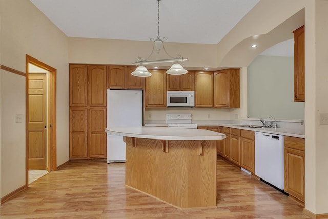 kitchen featuring white appliances, light wood finished floors, a kitchen island, light countertops, and a sink