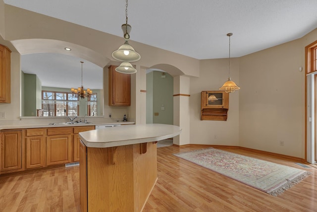 kitchen featuring a sink, light countertops, light wood finished floors, a kitchen bar, and pendant lighting