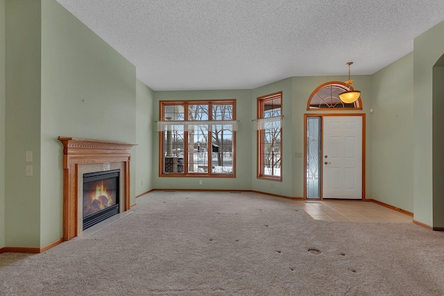 unfurnished living room with carpet floors, baseboards, a textured ceiling, and a glass covered fireplace