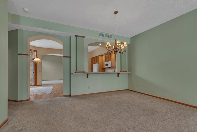 carpeted spare room with an inviting chandelier, baseboards, visible vents, and arched walkways