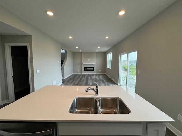 kitchen with recessed lighting, a sink, open floor plan, light countertops, and a glass covered fireplace