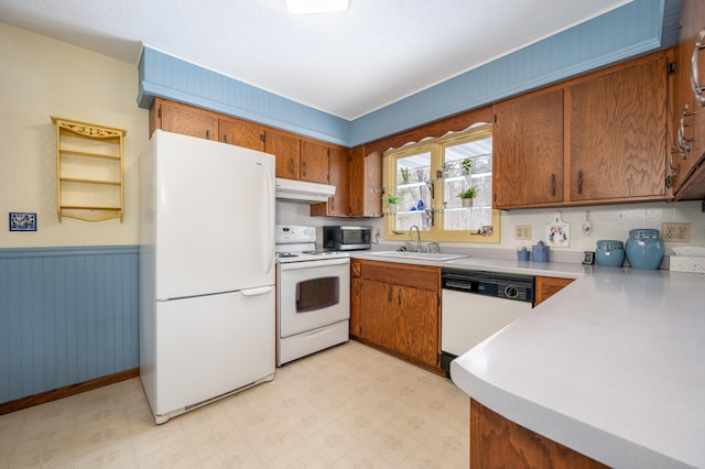 kitchen featuring white appliances, a wainscoted wall, light floors, under cabinet range hood, and a sink