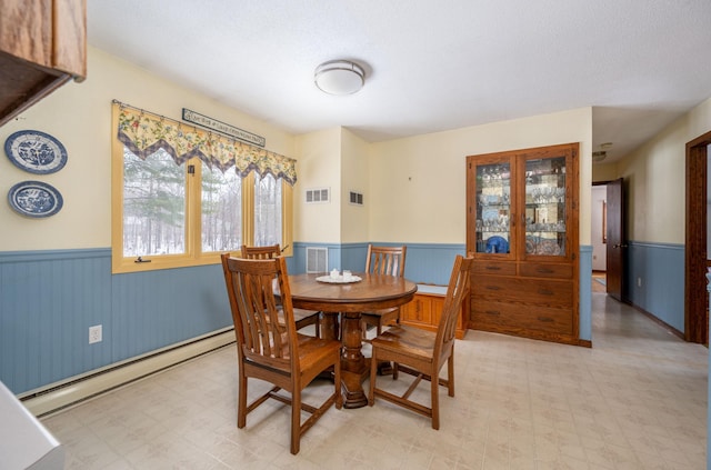 dining space featuring a baseboard heating unit, light floors, a wainscoted wall, and visible vents