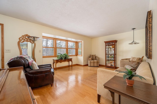 living area featuring baseboards, light wood-style flooring, and a textured ceiling