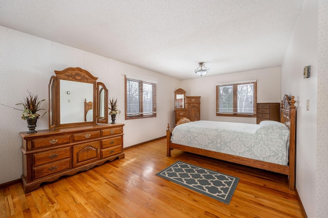 bedroom with a textured ceiling, light wood-type flooring, and baseboards