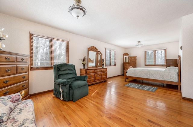 bedroom with a textured ceiling, light wood-type flooring, baseboards, and wallpapered walls