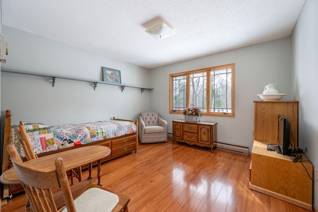 bedroom featuring light wood-style floors, a baseboard heating unit, baseboard heating, and a textured ceiling