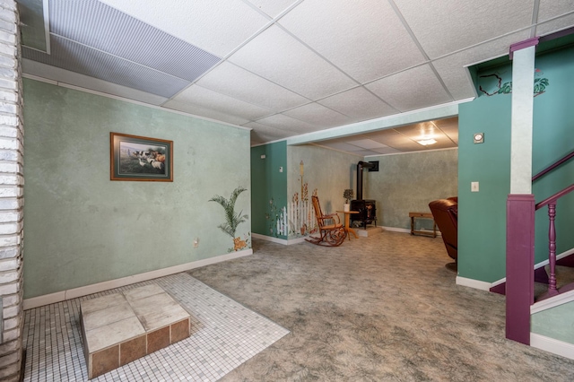 basement featuring a paneled ceiling, a wood stove, and baseboards