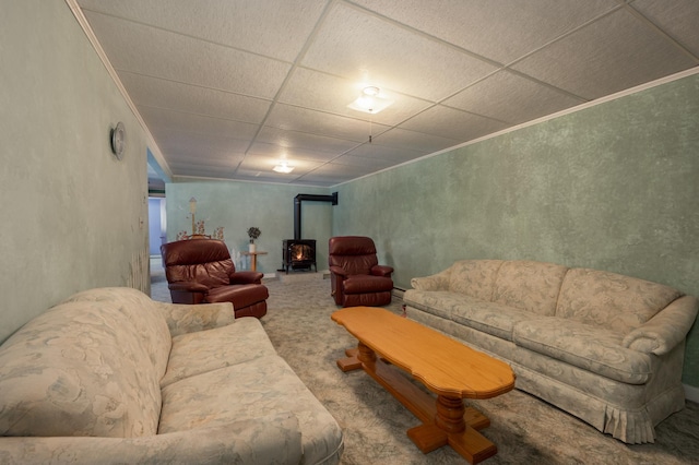 carpeted living area with a baseboard heating unit, a drop ceiling, a wood stove, and crown molding