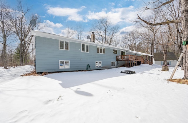 snow covered back of property with a chimney and a deck