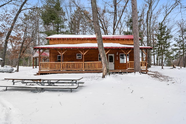 snow covered back of property with covered porch and metal roof