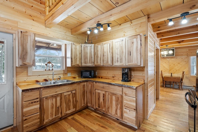 kitchen with beam ceiling, light wood-style flooring, a sink, wood walls, and black appliances