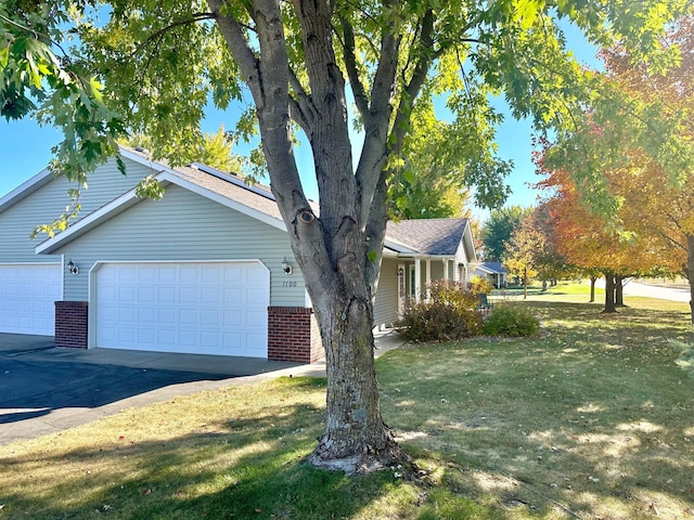 view of side of property featuring driveway, brick siding, a garage, and a yard