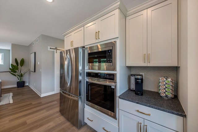 kitchen with a barn door, tasteful backsplash, baseboards, appliances with stainless steel finishes, and wood finished floors