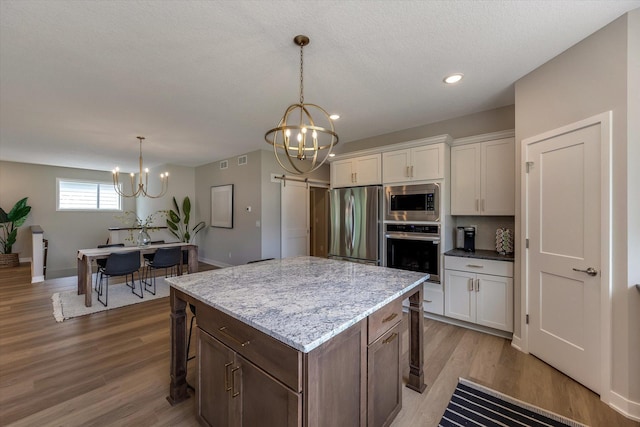 kitchen featuring a center island, an inviting chandelier, appliances with stainless steel finishes, white cabinetry, and wood finished floors