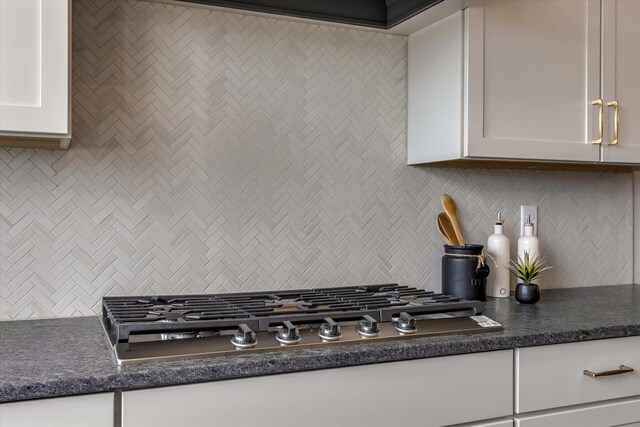 kitchen featuring dark countertops, tasteful backsplash, stainless steel gas cooktop, and white cabinets