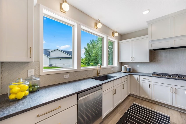 kitchen with stainless steel appliances, decorative backsplash, white cabinets, a sink, and light wood-type flooring