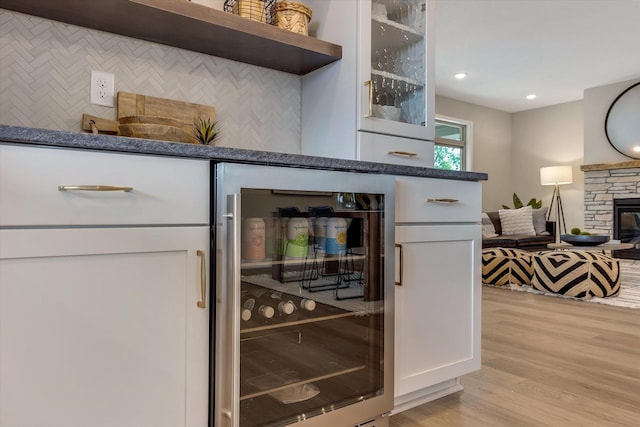 bar featuring light wood finished floors, decorative backsplash, wine cooler, a fireplace, and recessed lighting