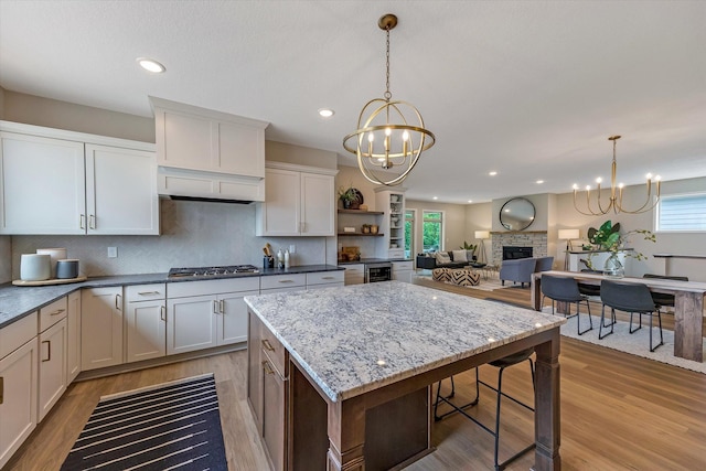 kitchen with light wood-type flooring, a notable chandelier, stainless steel gas cooktop, and a stone fireplace