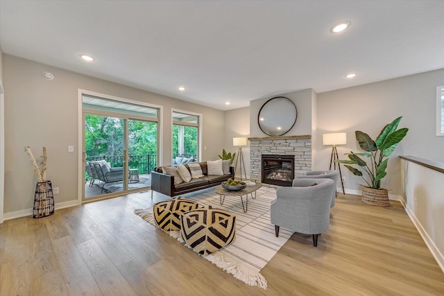 living room featuring baseboards, a stone fireplace, recessed lighting, and light wood-style floors