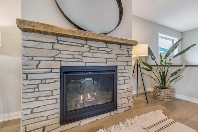 interior details with a stone fireplace, baseboards, and wood finished floors