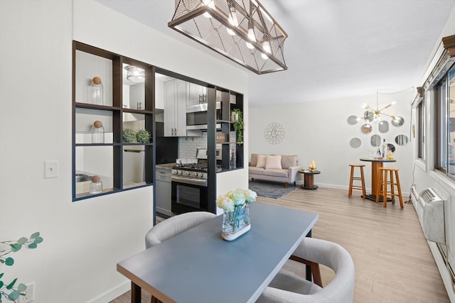 dining space with baseboards, light wood finished floors, an AC wall unit, and a notable chandelier