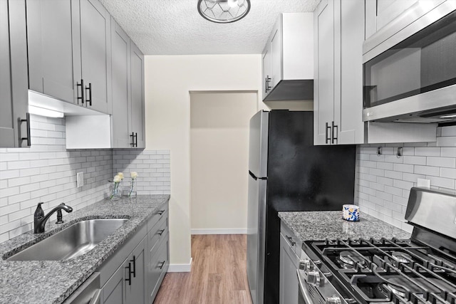 kitchen with backsplash, stainless steel appliances, light stone counters, and a sink