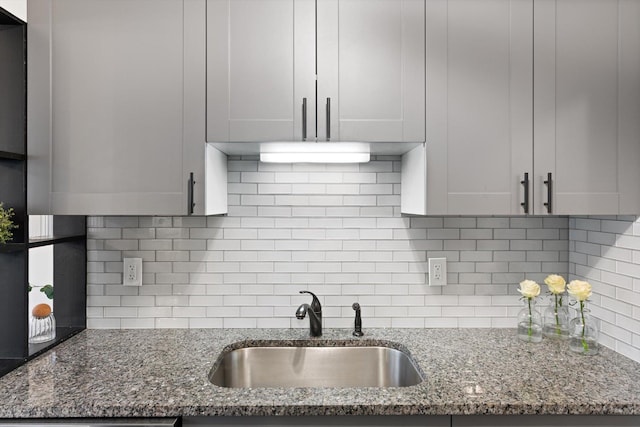 kitchen featuring stone countertops, decorative backsplash, and a sink