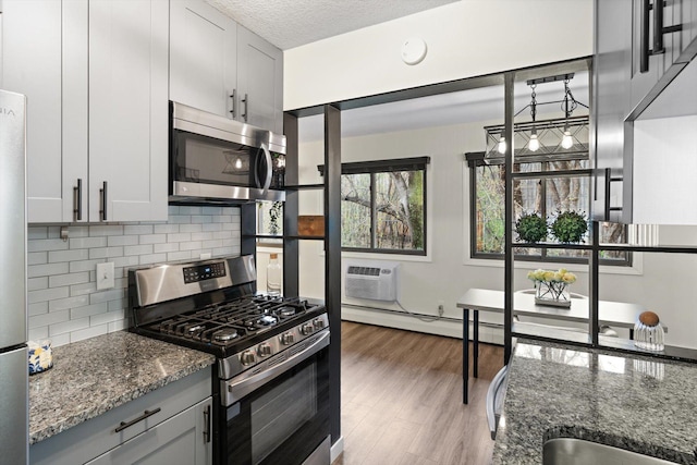 kitchen featuring baseboard heating, an AC wall unit, dark stone countertops, stainless steel appliances, and backsplash
