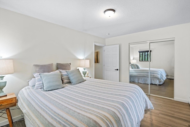 bedroom with a textured ceiling, baseboards, wood finished floors, and a closet
