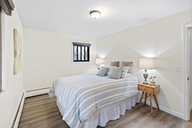 bedroom featuring wood finished floors, baseboards, and a baseboard heating unit