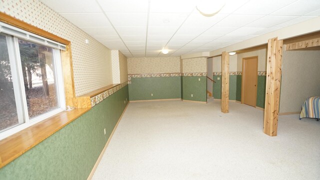 basement featuring baseboards, light colored carpet, a drop ceiling, and wallpapered walls