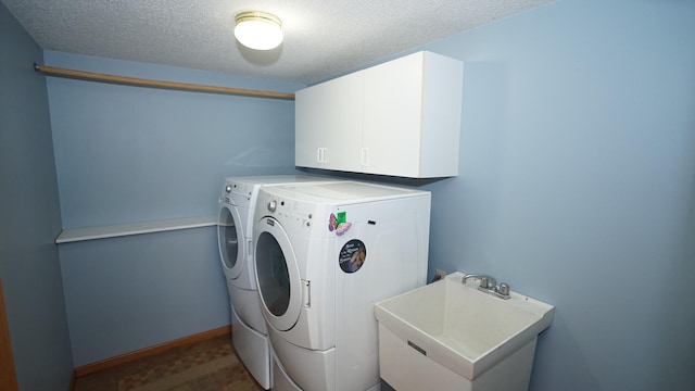 washroom featuring cabinet space, a sink, a textured ceiling, and washing machine and clothes dryer