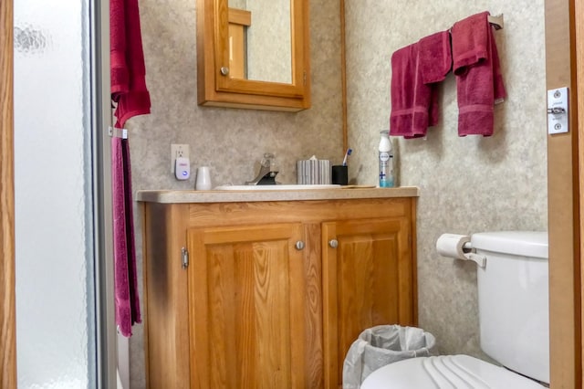 bathroom with toilet, vanity, and wallpapered walls