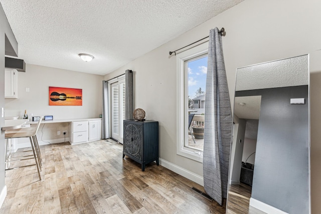 office space with visible vents, a textured ceiling, built in desk, light wood finished floors, and baseboards