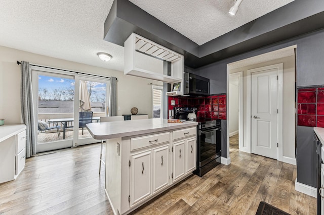 kitchen with stainless steel microwave, black / electric stove, light wood-style floors, a peninsula, and white cabinets