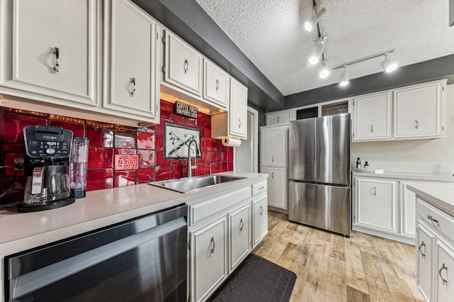 kitchen featuring light wood finished floors, freestanding refrigerator, a sink, light countertops, and dishwasher