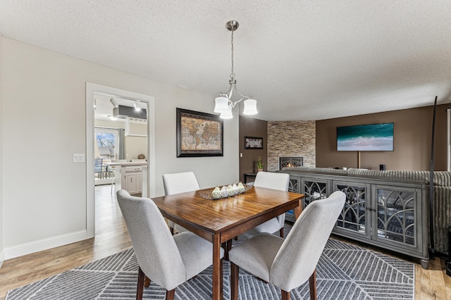 dining room with baseboards, a chandelier, a fireplace, wood finished floors, and a textured ceiling