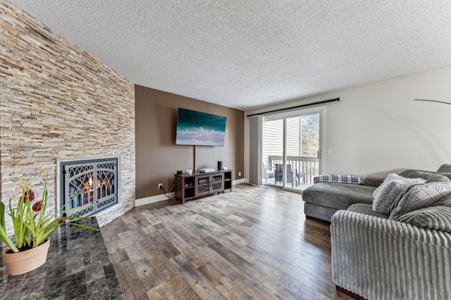 living area featuring baseboards, a textured ceiling, a stone fireplace, and wood finished floors