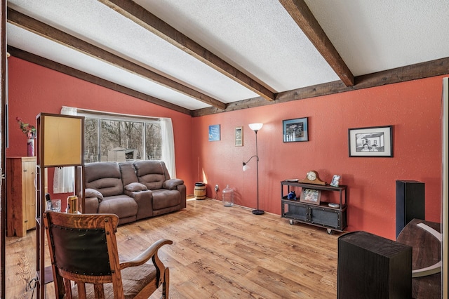 living room with a textured wall, lofted ceiling with beams, light wood finished floors, and a textured ceiling