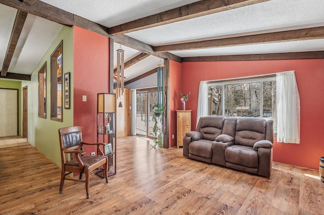 living area featuring vaulted ceiling with beams, a textured wall, a textured ceiling, and light wood-style flooring