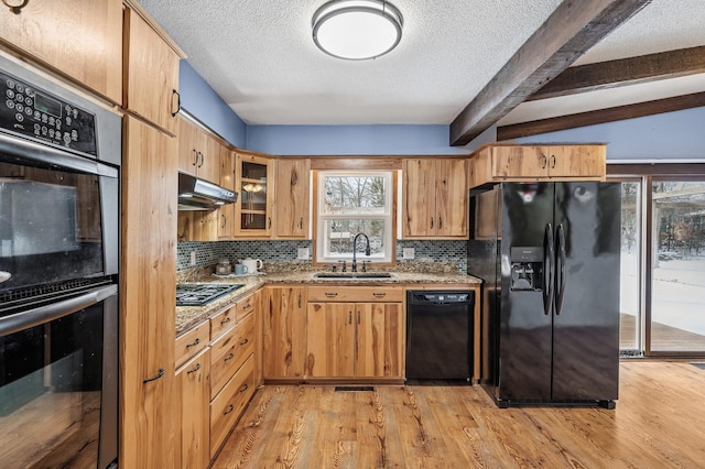 kitchen with black appliances, light wood-style flooring, under cabinet range hood, and a sink