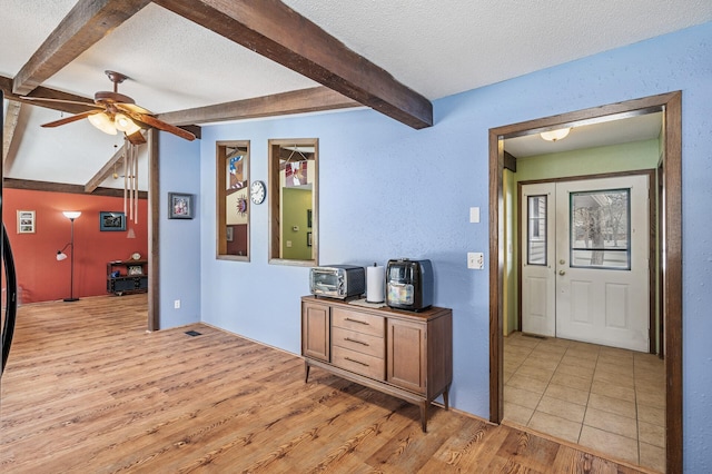 interior space with a textured ceiling, ceiling fan, beam ceiling, and light wood-style flooring