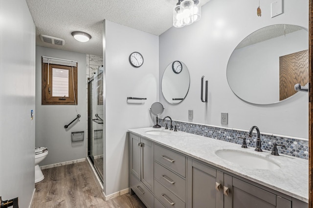 bathroom with a textured ceiling, visible vents, a sink, and wood finished floors