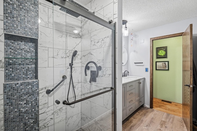 bathroom with a textured ceiling, wood finished floors, visible vents, vanity, and a stall shower