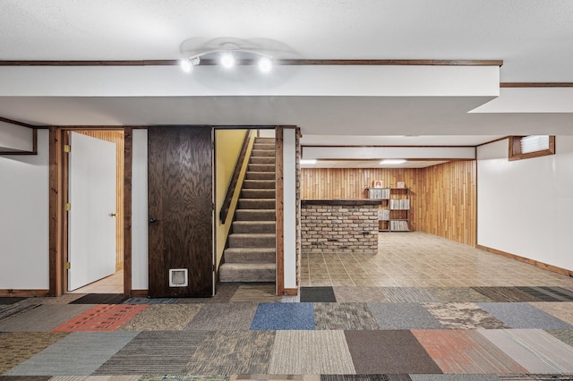 finished below grade area with stairs, baseboards, carpet flooring, and wooden walls