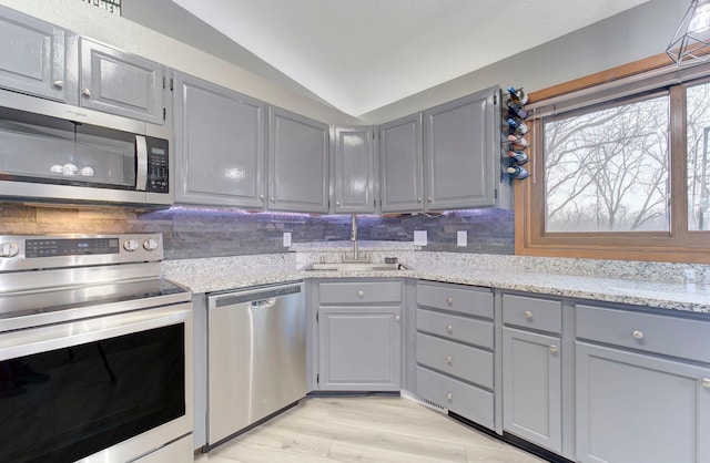 kitchen with decorative backsplash, gray cabinetry, appliances with stainless steel finishes, a sink, and vaulted ceiling