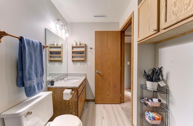 half bathroom with a textured ceiling, toilet, wood finished floors, vanity, and visible vents