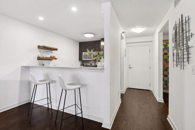 interior space featuring visible vents, dark wood finished floors, baseboards, stainless steel microwave, and a kitchen bar